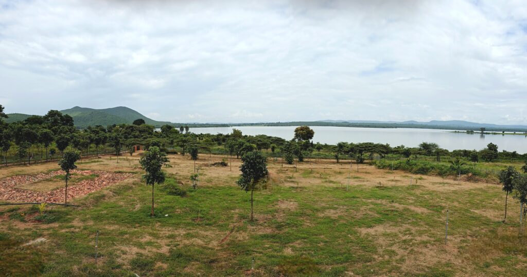 A scenic landscape featuring a lake, greenery, and distant hills under a cloudy sky.